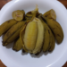Steamed Cambodian Chek Kramuon wax bananas arranged on a white plate over a wooden table, one banana peeled open to show its soft golden flesh.