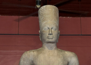 Sandstone Harihara statue from Phnom Da, a seventh-century fusion of Shiva and Vishnu, standing head reattached in the National Museum of Cambodia’s red-walled gallery in Phnom Penh