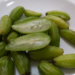 Fresh green bilimbi fruits on a white plate, with one fruit sliced open to show the pale, juicy interior and seeds.