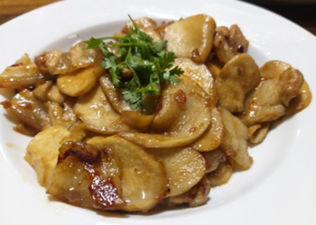 Close-up of Cambodian-style king oyster mushroom (ផ្សិតភ្លៅមាន់) sautéed with sliced pork on a white plate, garnished with fresh coriander, showing glossy, caramelized edges.