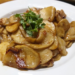 Close-up of Cambodian-style king oyster mushroom (ផ្សិតភ្លៅមាន់) sautéed with sliced pork on a white plate, garnished with fresh coriander, showing glossy, caramelized edges.