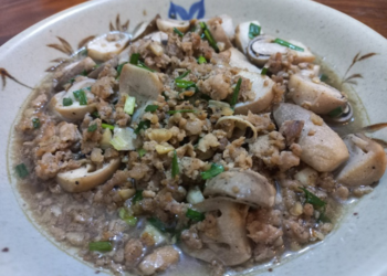 Close-up of a Cambodian-style dish featuring halved straw mushrooms sautéed with minced pork, garlic, and chopped scallions in a light savory broth, served in a ceramic bowl.