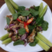 Lao-origin Cambodian deep-fried pork larb salad on a white plate, with cucumber spears, crispy pork pieces, red onion, fresh mint leaves, sliced red chilies, and a dusting of ground roasted rice.