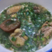 Close-up of a bowl of Cambodian ngam ngov chicken soup with preserved lime, tender chicken pieces, and chopped fresh herbs floating in a clear, aromatic broth.