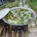 Traditional Cambodian num ansam sticky rice cakes wrapped in banana leaves steaming in outdoor cauldron over wood fire during Pchum Ben festival in countryside near Phnom Penh