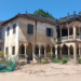 Abandoned two-story French colonial villa with arched verandas and peeling yellow walls under a bright blue sky in Angkor Borei, Takeo province, Cambodia.