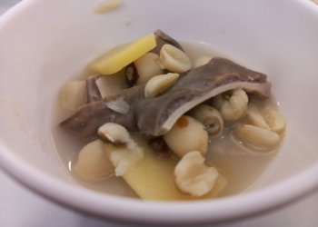 Close-up of Cantonese pickled vegetable pig stomach soup with ginger slices, lotus seeds, and tender offal pieces in a white bowl at Fisherman Quay Restaurant in Phnom Penh.