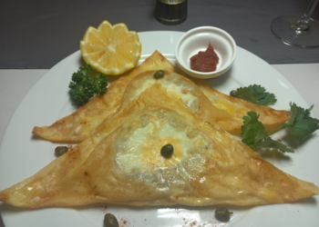 Triangular Tunisian brik on white plate filled with tuna and soft egg, garnished with capers, lemon wedge, parsley, and harissa — evoking childhood memories at Kilimandjaro restaurant Siem Reap