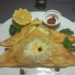 Triangular Tunisian brik on white plate filled with tuna and soft egg, garnished with capers, lemon wedge, parsley, and harissa — evoking childhood memories at Kilimandjaro restaurant Siem Reap