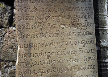 A close-up of a weathered sandstone door pillar at Prasat Krachap in Koh Ker, Cambodia, carved with lines of ancient Sanskrit script from a 928 CE inscription dedicating the temple to the deity Tribhuvanadeva