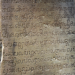 A close-up of a weathered sandstone door pillar at Prasat Krachap in Koh Ker, Cambodia, carved with lines of ancient Sanskrit script from a 928 CE inscription dedicating the temple to the deity Tribhuvanadeva