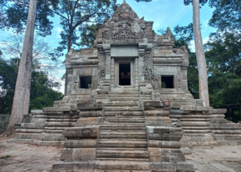 Stone stairway and restored sandstone sanctuary of Prasat Chom temple in the Preah Pithu group at Angkor Thom, Cambodia, framed by tall trees and surrounded by forest.