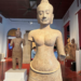 Angkor-era Bayon-style Prajnaparamita sandstone statue displayed in the National Museum of Cambodia after its 2024 return from the Denver Art Museum, with visitors viewing other Khmer sculptures in the gallery.