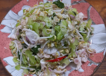 Plate of finely sliced Cambodian bitter melon salad mixed with shrimps, beansprouts, lemongrass, fresh herbs, and chili on a floral dish