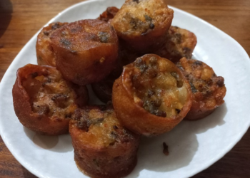 Plate of small round Cambodian pork trotter cakes (nom cheung chrouk), deep-fried to a golden brown, showing crisp edges and speckled peanuts.
