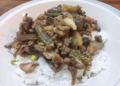 A plate of white rice topped with Cambodian stir-fried eggplant, mushrooms and minced pork.