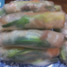 Close-up of stacked Cambodian fresh spring rolls (kuong) on a patterned blue plate, showing translucent rice paper wrapped around green herbs, pork, and shrimp.