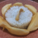 Close-up of Cambodian mango sticky rice served in a rustic clay bowl, with a round mound of glossy coconut sticky rice surrounded by golden mango slices like petals and a small jackfruit strip on top.