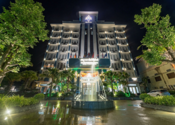 Night view of Kampong Thom Royal Hotel with bright facade lighting, central fountain and landscaped driveway framed by trees