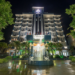 Night view of Kampong Thom Royal Hotel with bright facade lighting, central fountain and landscaped driveway framed by trees