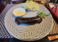 House-made blood sausage with mashed potatoes, mustard sauce, and greens served on a patterned plate at La Ferme de Bassac restaurant in Siem Reap.