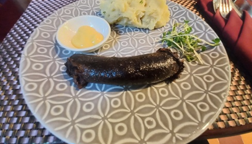 House-made blood sausage with mashed potatoes, mustard sauce, and greens served on a patterned plate at La Ferme de Bassac restaurant in Siem Reap.
