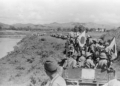 Japanese Imperial Army troops and supply wagons advancing along a dirt road through rural Indochina in 1940, with mountains visible in the background