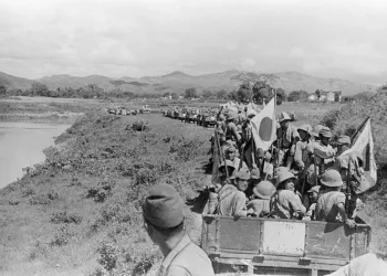 Japanese Imperial Army troops and supply wagons advancing along a dirt road through rural Indochina in 1940, with mountains visible in the background