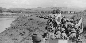 Japanese Imperial Army troops and supply wagons advancing along a dirt road through rural Indochina in 1940, with mountains visible in the background