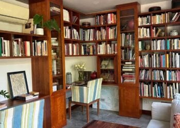Cozy corner of the Angkor Database Documentation Center with floor‑to‑ceiling wooden bookshelves, a striped chair, and a reading desk filled with books and maps.