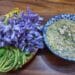 Plate of fresh and boiled Cambodian vegetables with purple edible flowers next to a bowl of chunky fresh shrimp dipping sauce (tuek kroeung bangkea) on a wooden table.Plate of fresh and boiled Cambodian vegetables with purple edible flowers next to a bowl of chunky fresh shrimp dipping sauce (tuek kroeung bangkea) on a wooden table.