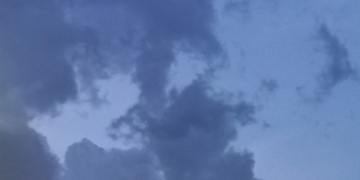 Stormy evening sky over Kampong Thom, Cambodia, with dark monsoon clouds drifting across a blue twilight background above village rooftops.