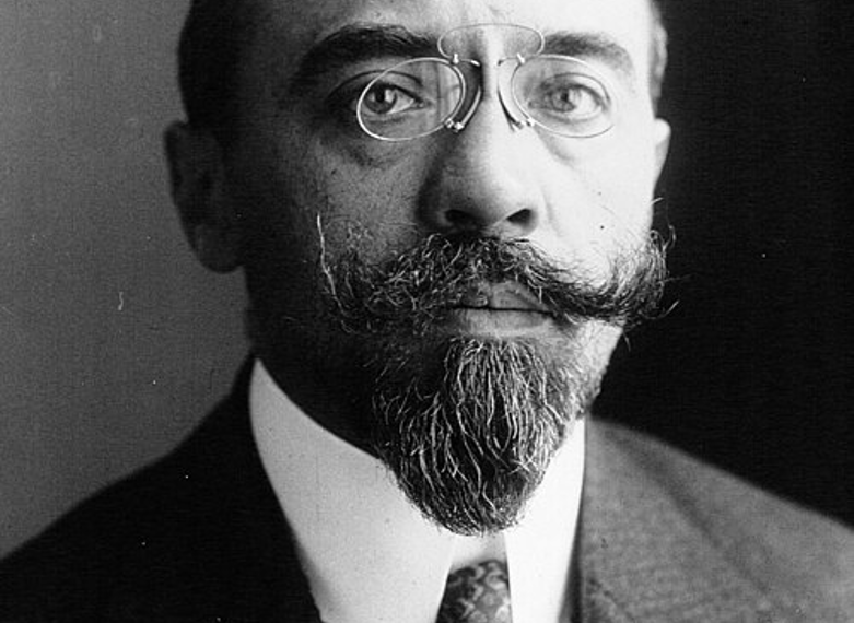 Black‑and‑white studio portrait of Albert Sarraut in 1914, shown from the chest up in a dark suit, white shirt and patterned tie, facing the camera against a plain, dark background.