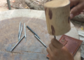 Close-up of a Siem Reap artisan using metal chisels and a wooden mallet on a leather panel to create traditional sbaek thom Khmer shadow puppets.