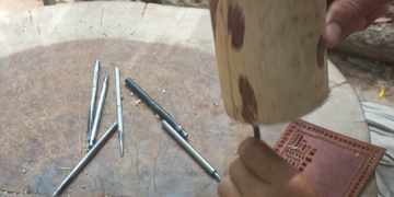 Close-up of a Siem Reap artisan using metal chisels and a wooden mallet on a leather panel to create traditional sbaek thom Khmer shadow puppets.