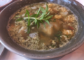 Close-up of a ceramic bowl filled with Cambodian sour fish soup (samlor machu trey) with fish roe, herbs, and vegetables, served at Kraya Angkor restaurant in Phnom Penh.