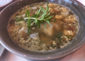 Close-up of a ceramic bowl filled with Cambodian sour fish soup (samlor machu trey) with fish roe, herbs, and vegetables, served at Kraya Angkor restaurant in Phnom Penh.