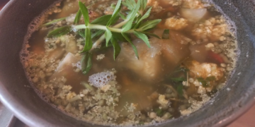 Close-up of a ceramic bowl filled with Cambodian sour fish soup (samlor machu trey) with fish roe, herbs, and vegetables, served at Kraya Angkor restaurant in Phnom Penh.