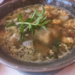 Close-up of a ceramic bowl filled with Cambodian sour fish soup (samlor machu trey) with fish roe, herbs, and vegetables, served at Kraya Angkor restaurant in Phnom Penh.