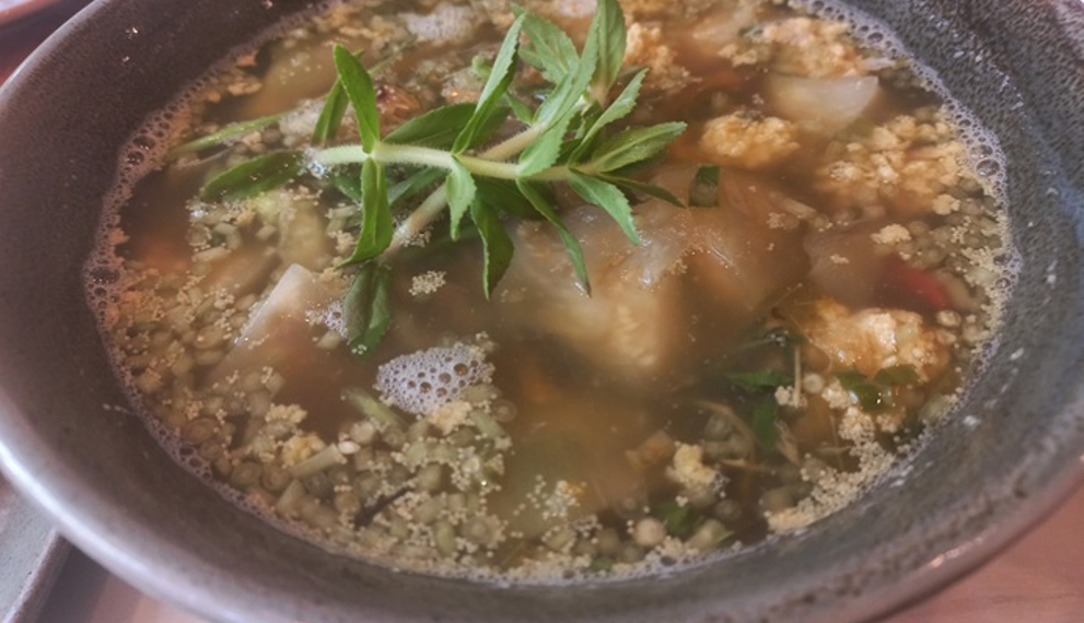 Close-up of a ceramic bowl filled with Cambodian sour fish soup (samlor machu trey) with fish roe, herbs, and vegetables, served at Kraya Angkor restaurant in Phnom Penh.