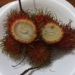 Close-up of opened red rambutans on a white plate in Phnom Penh, showing translucent flesh and playful “smiling” shapes, a typical Cambodian tropical fruit snack.