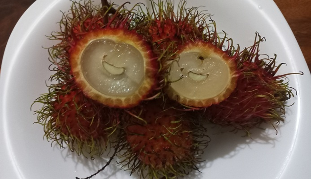 Close-up of opened red rambutans on a white plate in Phnom Penh, showing translucent flesh and playful “smiling” shapes, a typical Cambodian tropical fruit snack.