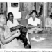 Black and white photo of monk Khieu Chum speaking at a table with three journalists in a simple indoor setting
