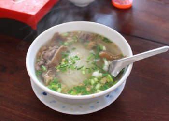 Steaming bowl of Cambodian kuy teav duck noodle soup at Phteah Bei Lveng in Battambang, with rice noodles, sliced duck, and green onions on a wooden table.