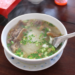 Steaming bowl of Cambodian kuy teav duck noodle soup at Phteah Bei Lveng in Battambang, with rice noodles, sliced duck, and green onions on a wooden table.