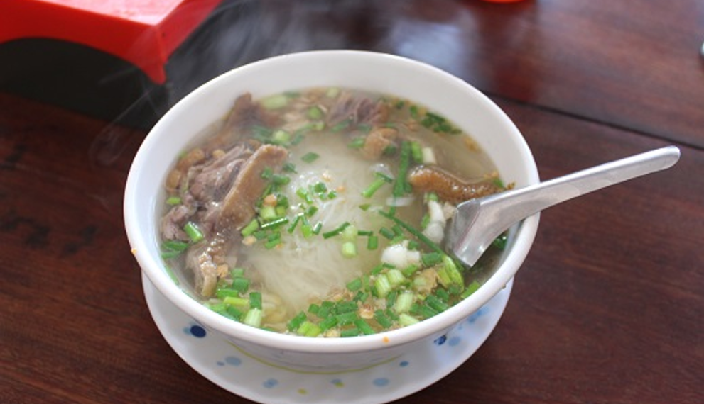 Steaming bowl of Cambodian kuy teav duck noodle soup at Phteah Bei Lveng in Battambang, with rice noodles, sliced duck, and green onions on a wooden table.