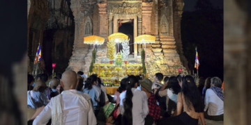 De nuit, au temple de Lolei dans la province de Siem Reap, un groupe de fidèles assis sur des nattes fait face à un ancien sanctuaire en briques illuminé, décoré de parasols jaunes, de fleurs et d’offrandes, en attendant le moment précis fixé par la position de la lune pour lancer une cérémonie de la Fête de l’Eau.