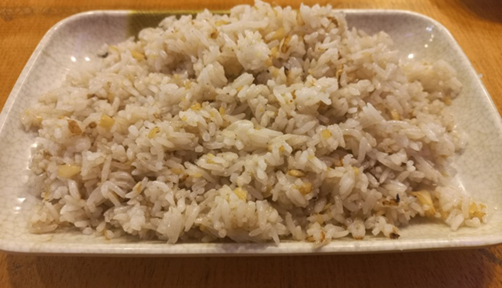 Rectangular plate of Cambodian rice sautéed with finely chopped garlic, served on a wooden table in a small Kampong Thom street restaurant.
