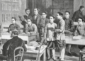 Black and white illustration of a classroom at the École cambodgienne in Paris, showing Cambodian male students in traditional garments standing and sitting at wooden desks while two European teachers supervise the lesson from the front and back of the room.
