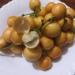 Close‑up of ripe yellow Burmese grapes (Baccaurea ramiflora, ផ្ញៀវ) on a white plate, one fruit opened to reveal its pale, juicy sweet‑sour flesh.